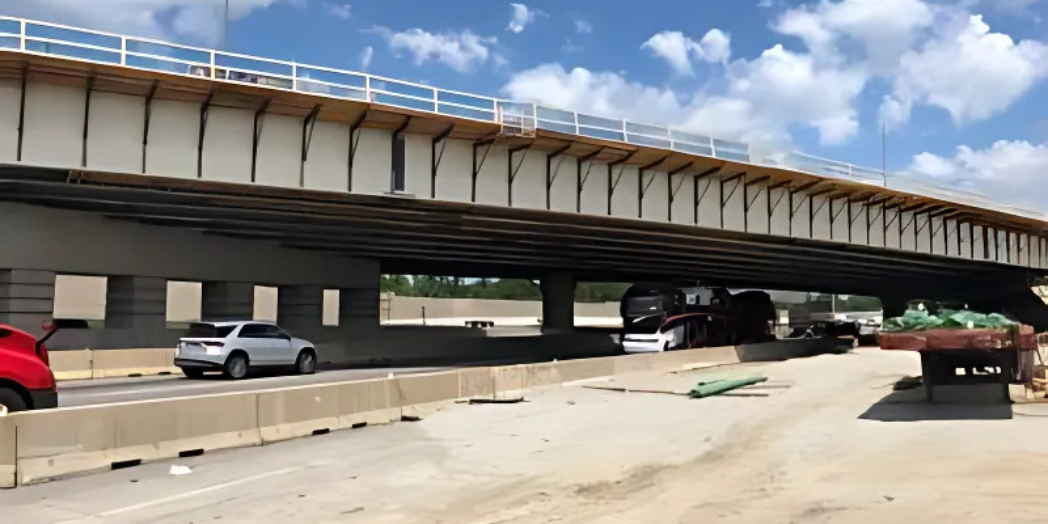 This image shows a newly constructed bridge over a highway during daytime.