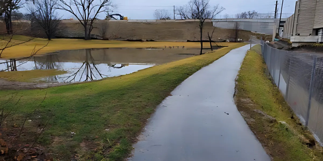 This image captures a wet paved pathway next to a fenced-off area, possibly near a highway construction site.