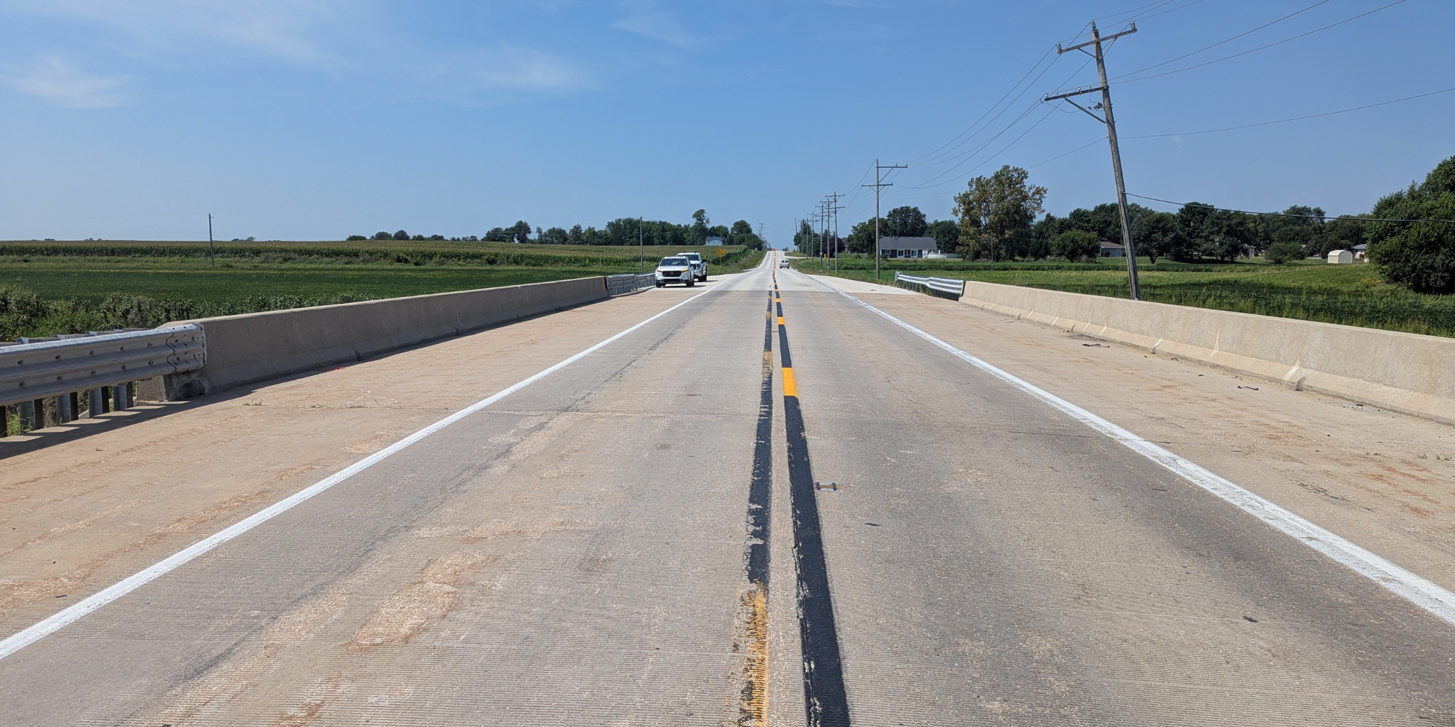 Existing County Line Road bridge deck showing pavement wear, lane markings, concrete barriers, and approaching vehicles.