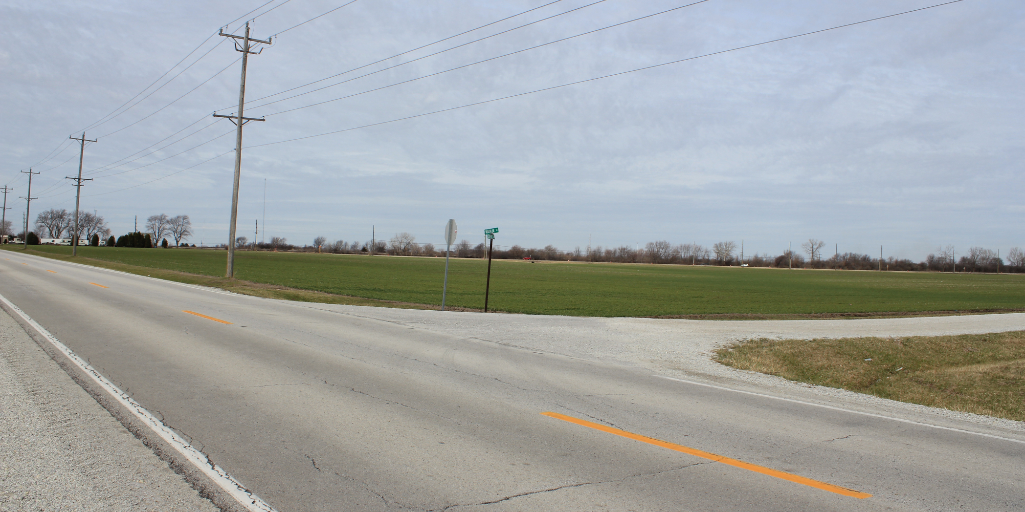 Rural intersection along County Line Road with a stop sign, gravel shoulders, utility lines, and adjacent farmland.