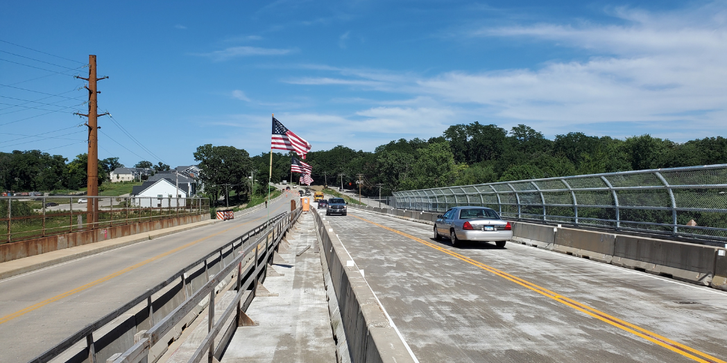 Vehicles cross Plainfield Road bridge beside concrete barriers separating traffic from the adjacent construction area.