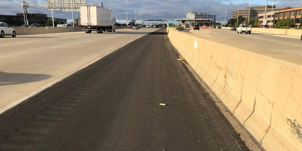 Resurfaced asphalt shoulder beside the concrete median barrier on I-88, with traffic traveling in both directions.