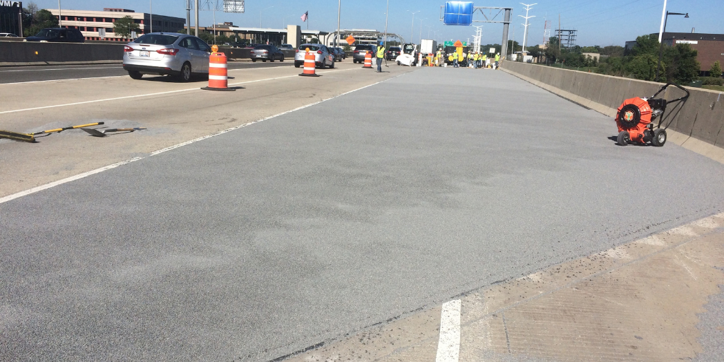 Newly applied gray bridge deck overlay on I-88, with construction barrels separating the work area from traffic.