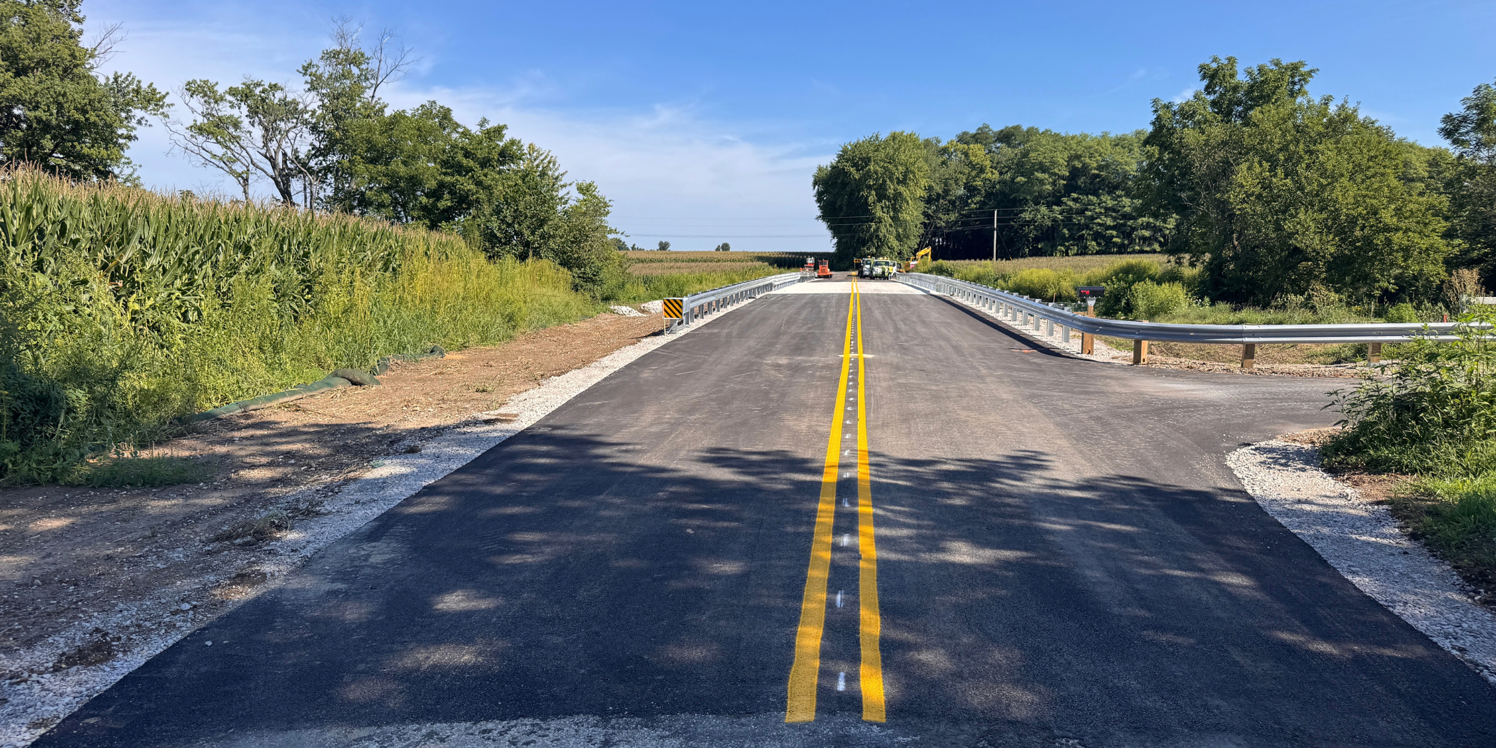 Newly paved County Road 400 W approaches Bridge No. 109, with double yellow centerlines, guardrails, and construction equipment ahead.