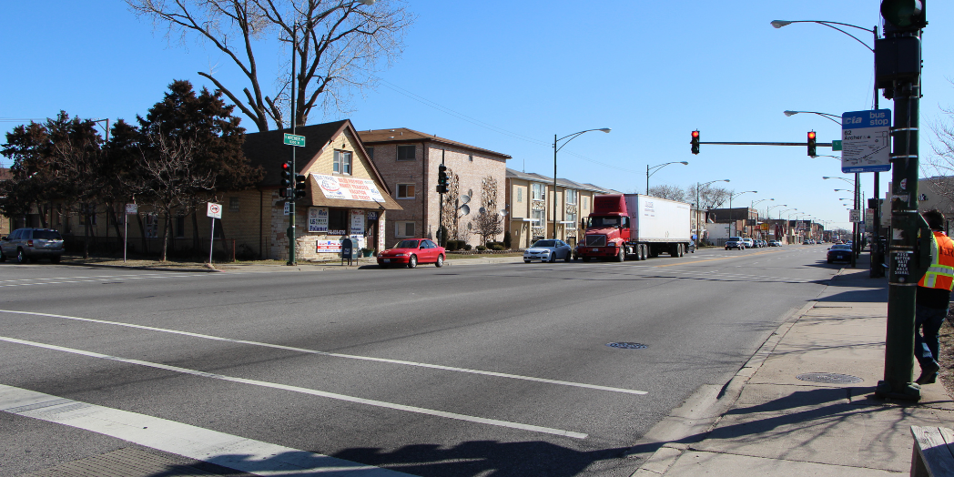 Cars and a semi-truck at a signalized intersection on Archer Avenue in Chicago, with marked crosswalks, sidewalks, and a CTA bus stop.