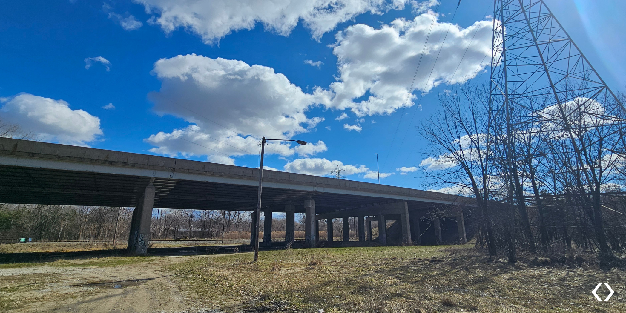 View of the completed US-131 bridge rehabilitation in Grand Rapids, with concrete support piers, railroad tracks below, and a transmission tower beside the bridge.