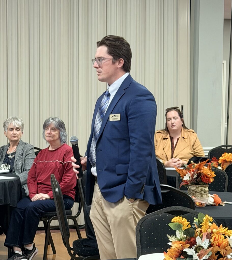 John Buchanan of the Kentucky League of Cities holds a microphone while presenting to seated attendees.
