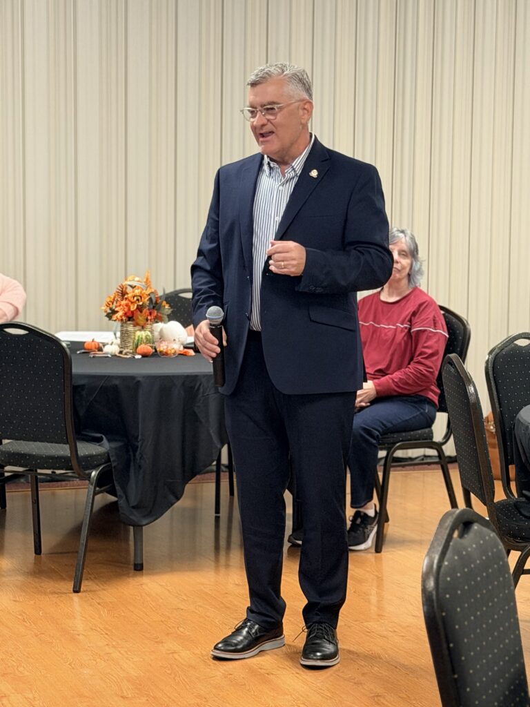 Kentucky Senator Robby Mills holds a microphone while addressing attendees at a Sturgis gathering.
