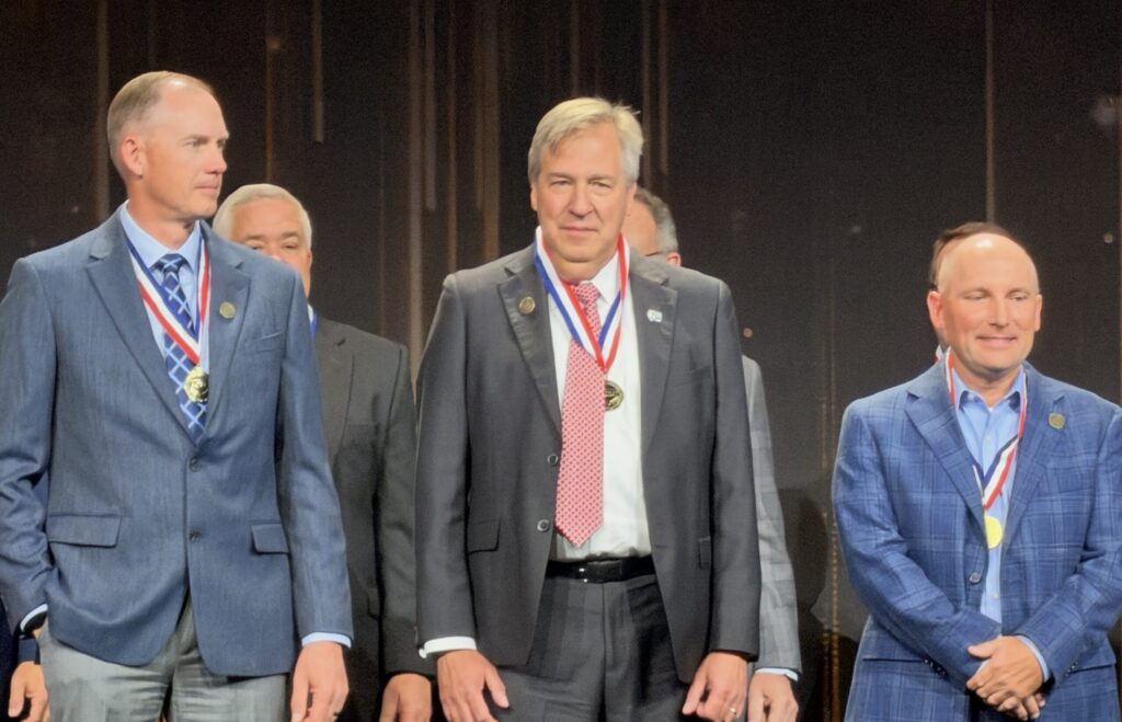 Jerry Payonk, PE, stands at center in a dark suit and red tie, wearing his induction medal alongside other ACEC honorees.